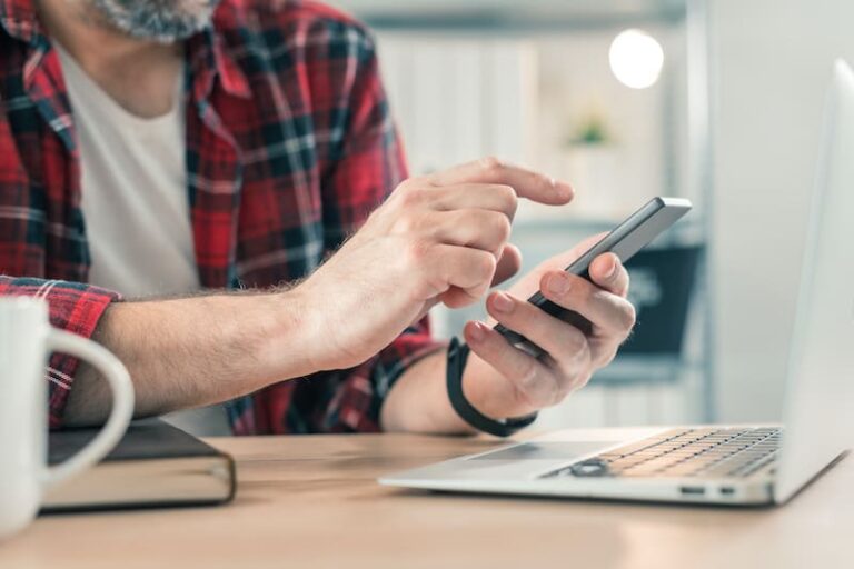 Un homme avec une chemise à carreau a son téléphone dans les main et complète son dossier