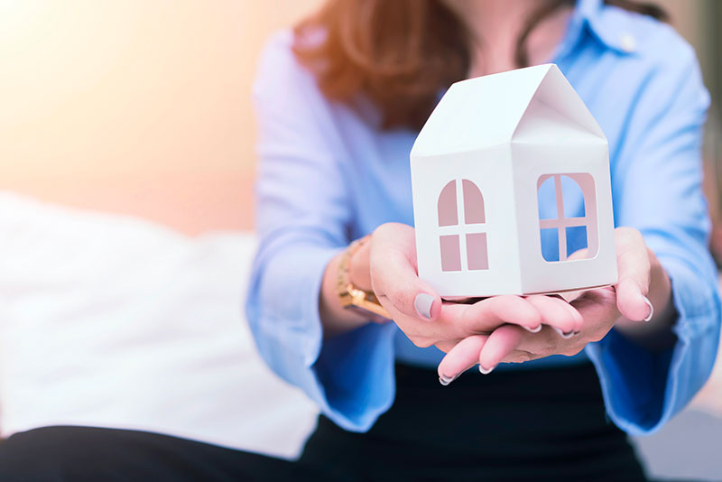 Une femme avec une chemise bleu assise sur un canapé tient une maison blanche dans ses mains
