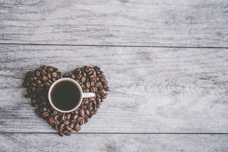 Sur des planches de bois grise, un tas de grain de café en forme de coeur avec une tasse de café