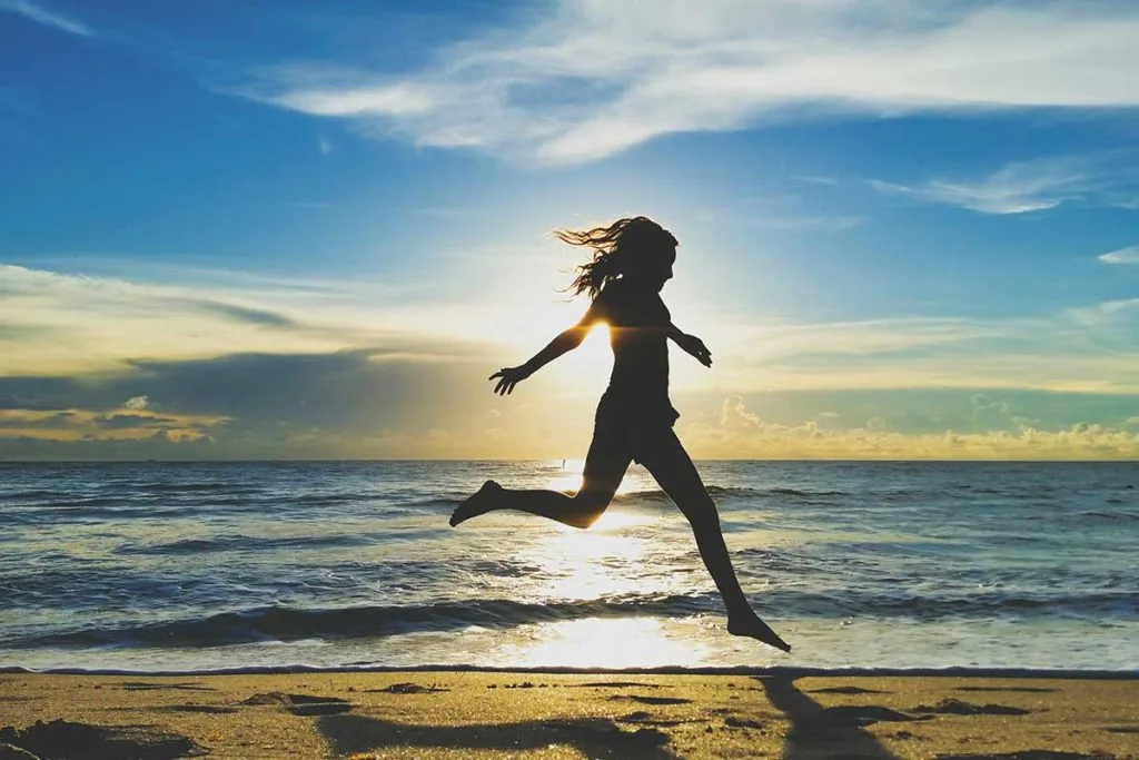 Une femme saute en l'aire sur la plage avec le soleil couchant derriere