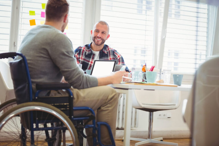 Un homme en fauteuil parle à un autre homme assis derrière une table
