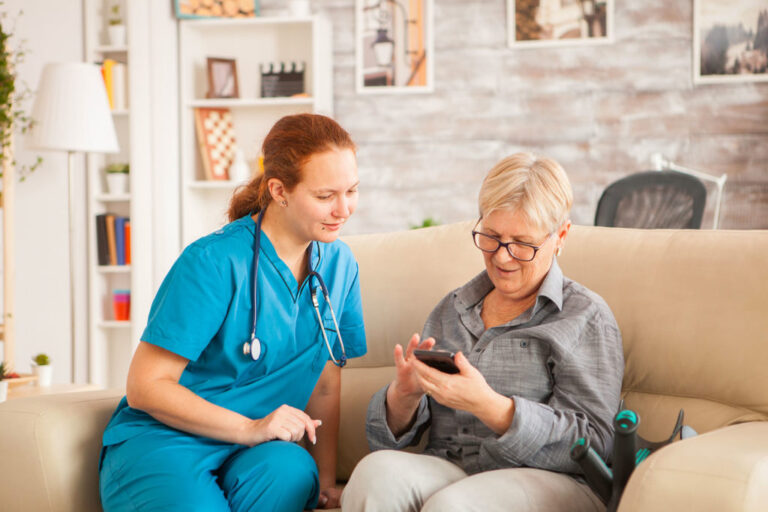 Une infirmière est assise à cote d'une femme senior, elle regarde une information sur le téléphone