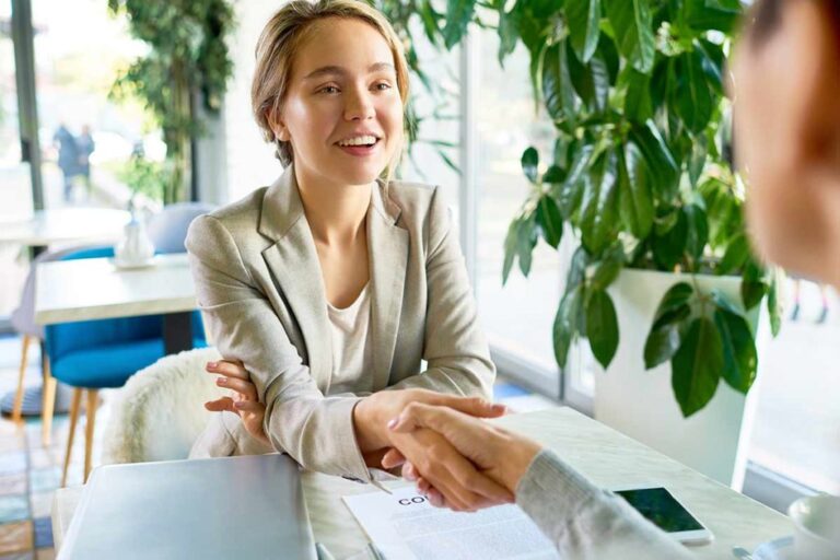 Une femme souriante assise à une table de café, serre la main à une femme face à elle